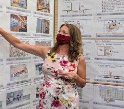 Person pointing to cork board with papers and photos