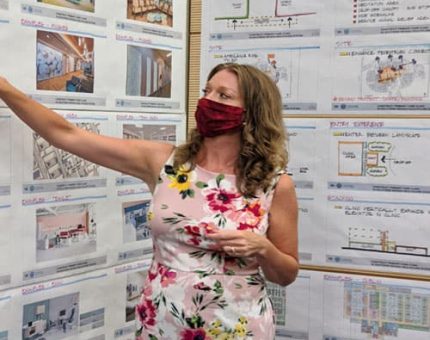 Person pointing to cork board with papers and photos